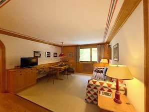 A cozy room with a television, a dining table, a sofa, and a lamp.