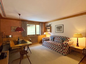 A cozy living room with a dining table, a patterned sofa, a lamp, and a radiator.