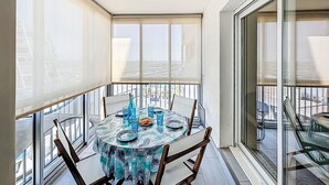 En balkon med et rundt spisebord, store vinduer med udsigt over byen og et gelænder af glas.