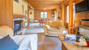 Un interior de cabaña acogedor con chimenea, un sofá, un comedor y un televisor.