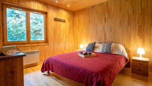 Dormitorio con paneles de madera, una cama grande, dos lámparas de noche y una ventana con vistas a árboles.