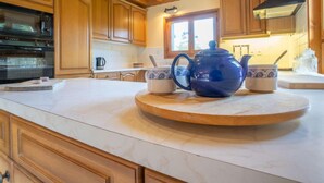 Una cocina con armarios de madera, una isla redonda de mármol, un hervidor azul y una tetera.
