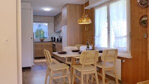 A dining area with a table set for four, surrounded by wicker chairs, a patterned rug, and a pendant light. - Salzhubelweg by Interhome (Goldswil)