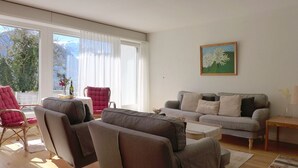 A living room with a grey sofa, two armchairs, a small table, and a window with sheer curtains. - Salzhubelweg by Interhome (Goldswil)
