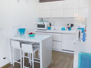 Una cocina compacta con armarios blancos, una pequeña isla con taburetes, un microondas, una licuadora y un tostador.