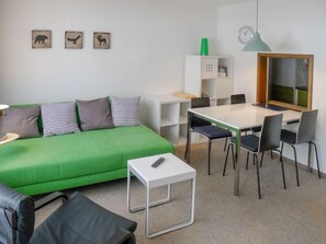Una habitación moderna con un sofá verde, una mesa blanca y cuatro sillas. Hay tres cuadros de animales colgados en la pared.