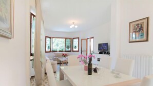 A dining area with a white table and chairs, a vase with flowers, and a television in the background. - Vacation home Sandra by Interhome (Forte dei Marmi)