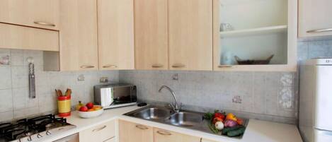 Una cocina con armarios de madera clara, un lavamanos de acero inoxidable, una estufa a gas, un tostador y un lavavajillas.