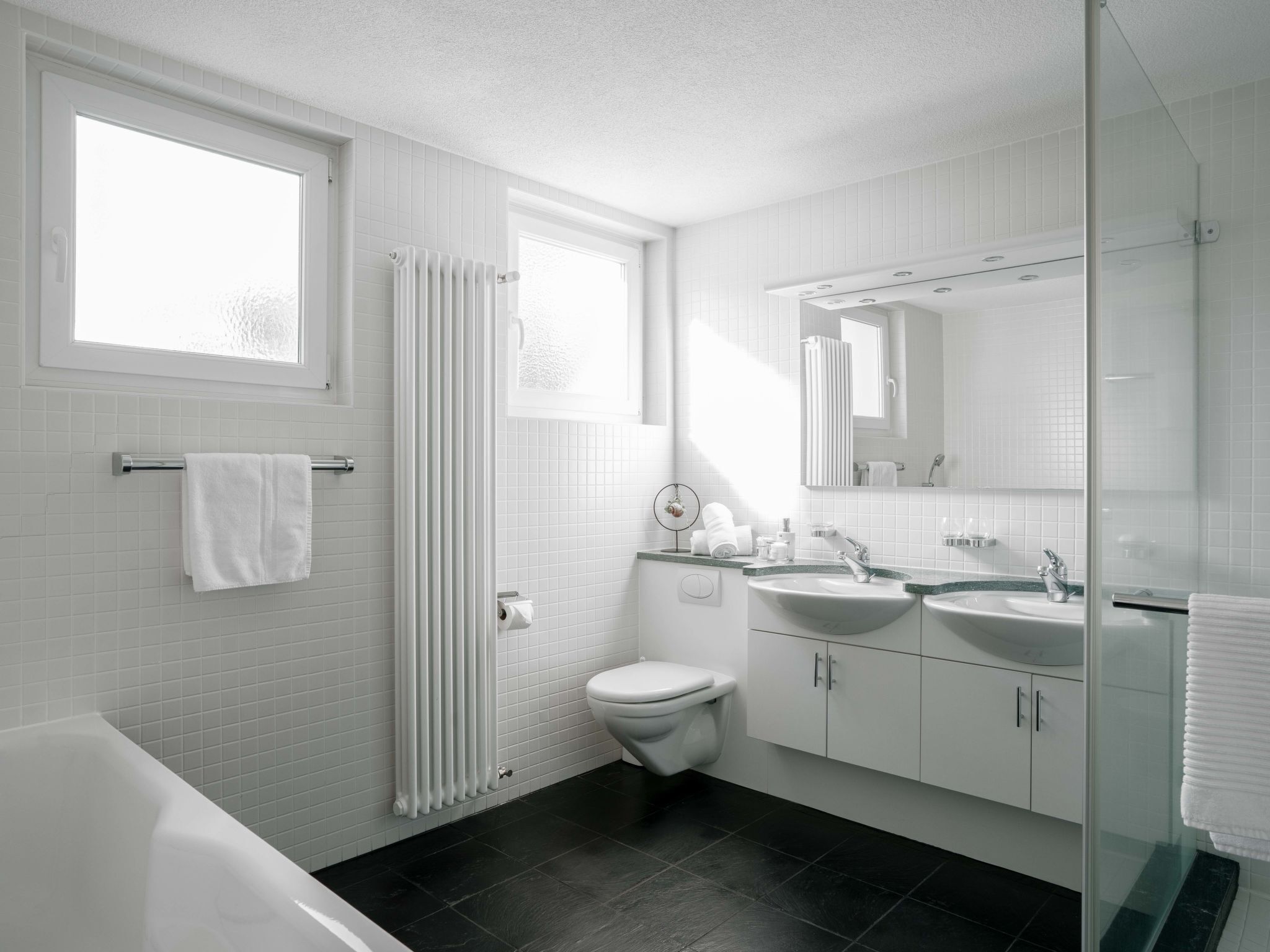 Un baño moderno con una bañera, dos lavamanos, un inodoro y un espejo grande.