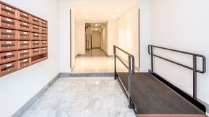 Un pasillo moderno con suelo de mármol, un mueble de almacenamiento de madera a la izquierda y una barandilla de metal a la derecha.