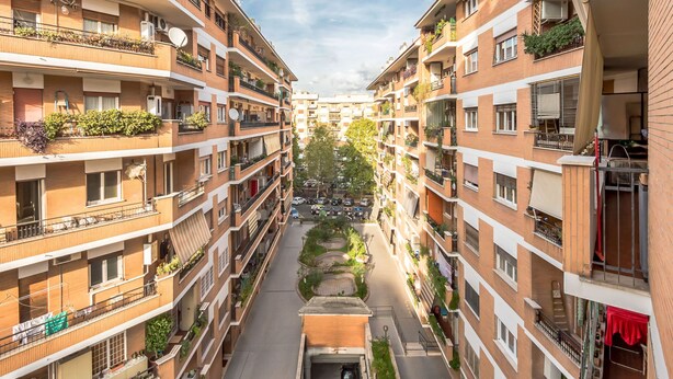 Un edificio residencial de varios pisos con balcones, un patio central y vista a la calle.