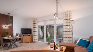 Un salon moderne comprenant un canapé, une table basse avec des collations, un téléviseur et un coin repas avec une table et des chaises.