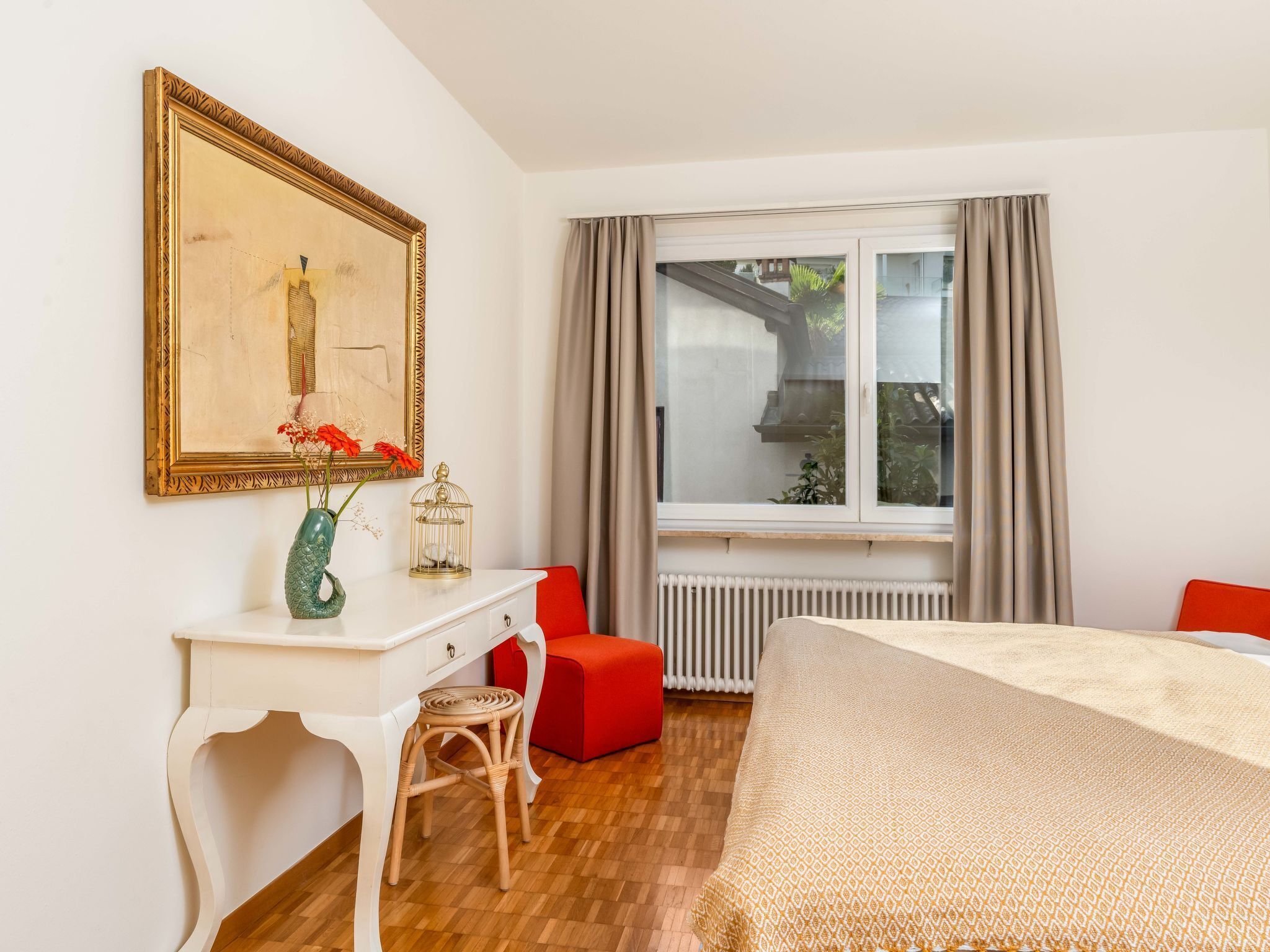 A bedroom with a bed, a desk, a chair, a window with curtains, and a radiator.
