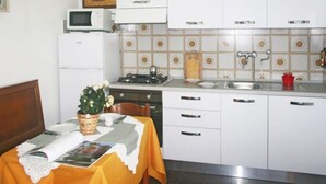 Una cocina con armarios blancos, estufa, microondas y fregadero. Hay una mesa de comedor con mantel amarillo y un cesto de flores.