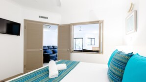 A hotel room with a bed, a blue patterned pillow, a white towel, a blue patterned bedspread, a television on the wall, and a window with a view of the outside. - THE REGAL - APARTMENT WITH SPA BATH - PRIME LOCATION IN TOWN CENTRE (Port Douglas)