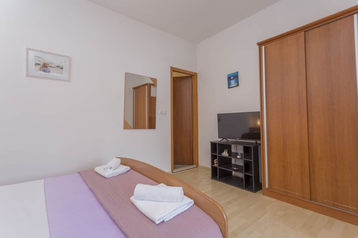A bedroom with a bed, a TV, a wardrobe, and a mirror.