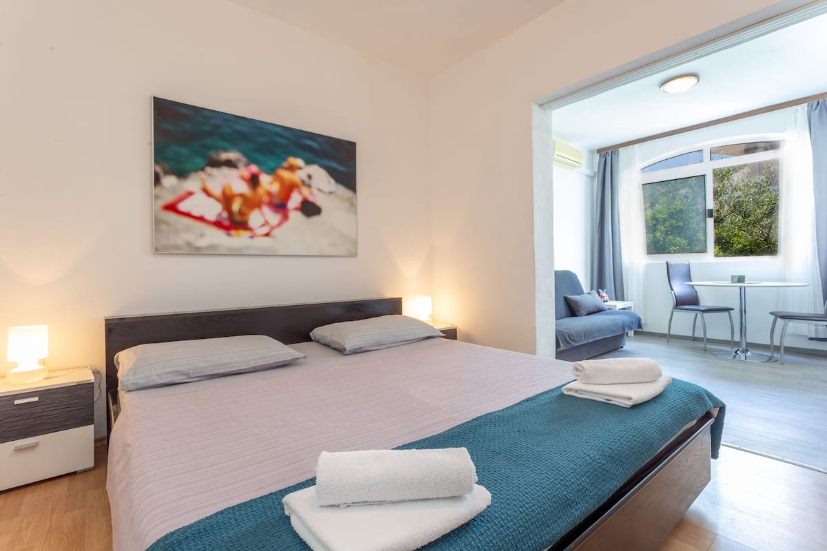 A modern hotel room with a large bed, a desk, and a view of the outdoors.