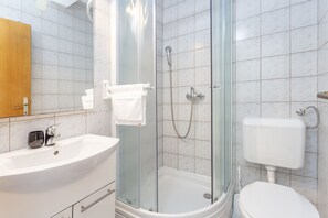 A bathroom with a glass-enclosed shower, a white sink, and a toilet. - Apartments Milka (Hvar)