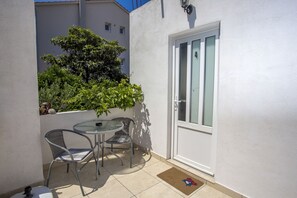A small outdoor patio with a round table and two chairs, a door with frosted glass panels, and a potted plant. - Apartments Milka (Hvar)