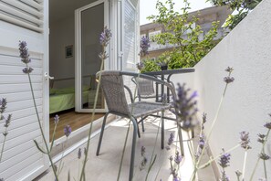 A balcony with wicker chairs and a table, overlooking a garden with lavender plants. - Apartments Milka (Hvar)
