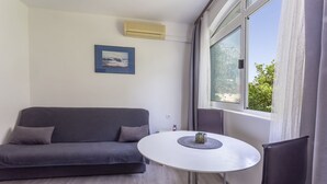 A modern living room with a grey sofa, a small round table, and a window with curtains. - Apartments Milka (Hvar)