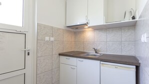 A compact kitchen with white cabinets, a built-in dishwasher, and a countertop sink. - Apartments Milka (Hvar)