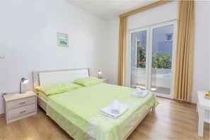 A neatly arranged bedroom with a bed, bedside table, lamp, and a view of the outdoors through a sliding glass door. - Apartments Milka (Hvar)