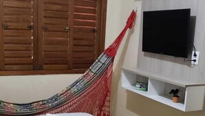 Une chambre à coucher avec un lit, un hamac, un téléviseur posé sur une étagère et une armoire.