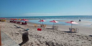 A beach with rows of beach chairs and umbrellas, a lifeguard stand, and a clear view of the ocean. - Pousada Casarão do Mar (Tibau)