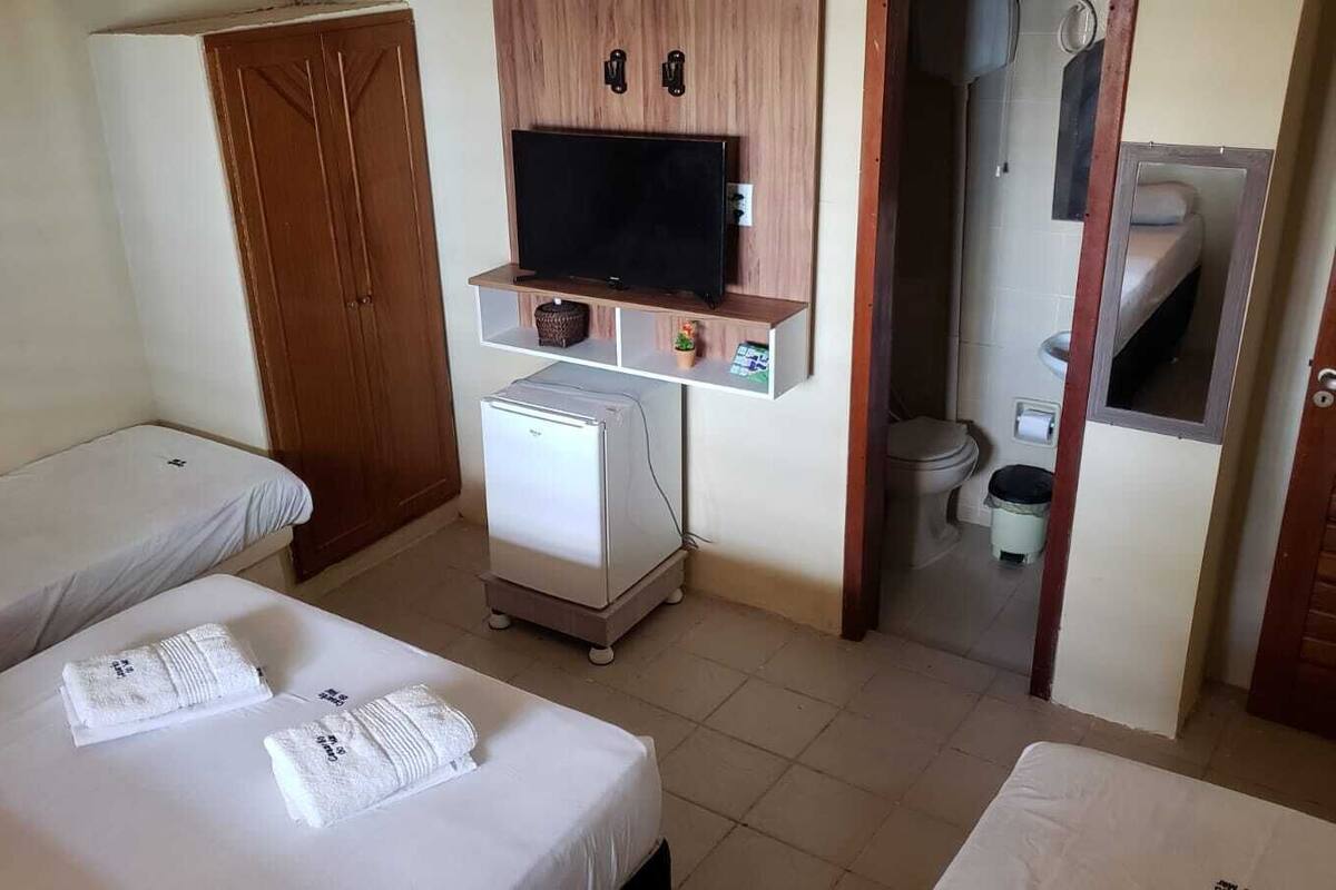 Quarto de hotel com duas camas, televisão, um pequeno frigorífico e casa de banho visível através de uma porta aberta.