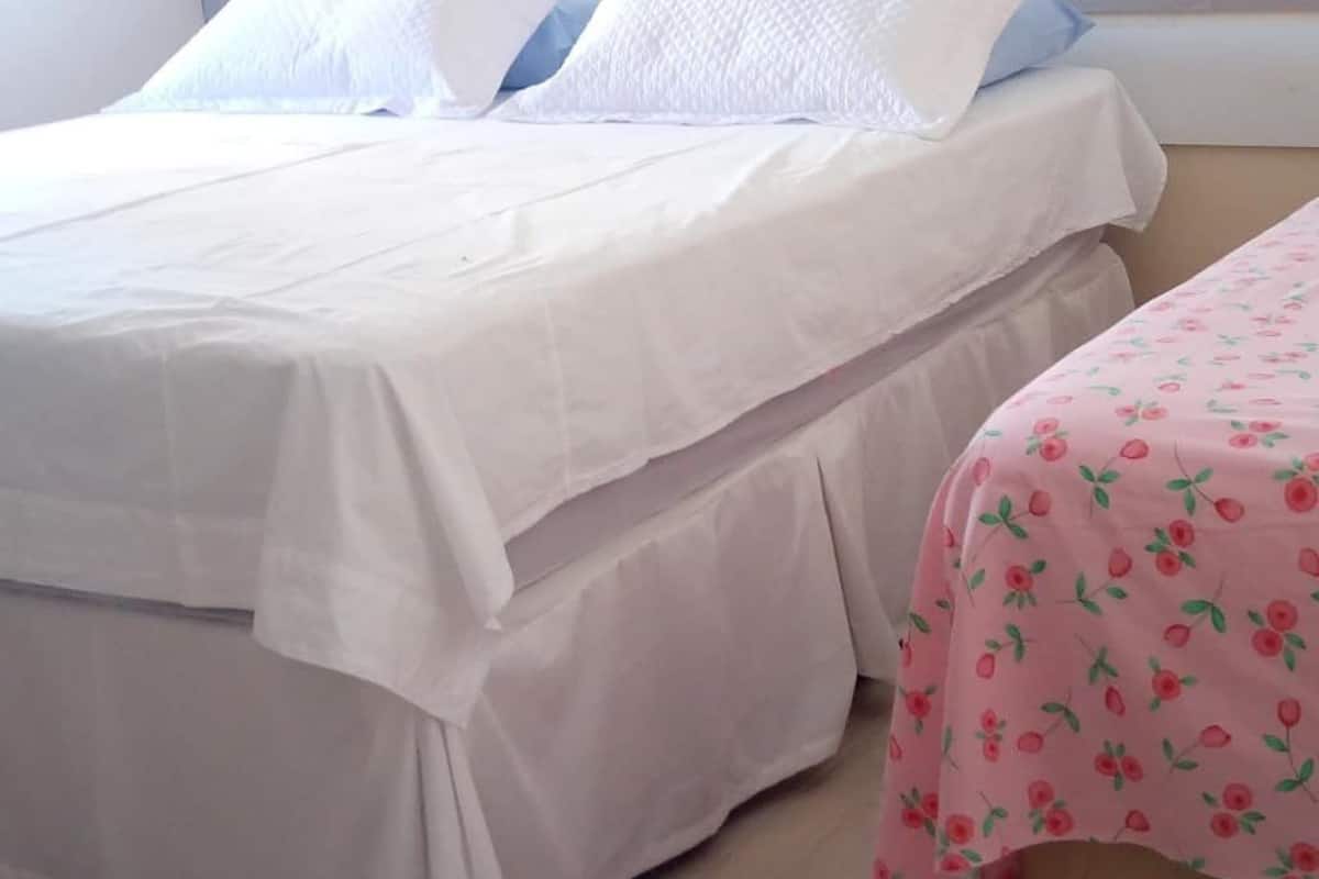 Cama com roupa de cama branca e um cobertor rosa estampado com cerejas.