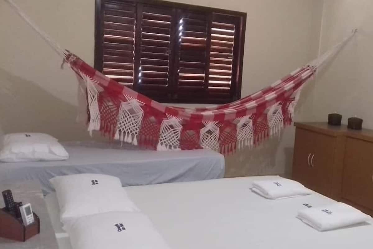 Quarto com duas camas, um guarda-roupa de madeira, televisão na parede e janela com persianas.