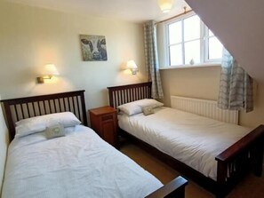 A room with two single beds, a small wooden nightstand, a wall-mounted lamp, and a window with curtains. - The Harp Inn (Hereford)
