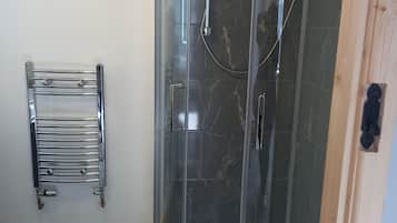 Une douche fermée par des parois en verre, dotée d’un pommeau de douche à main et d’une brosse à main.