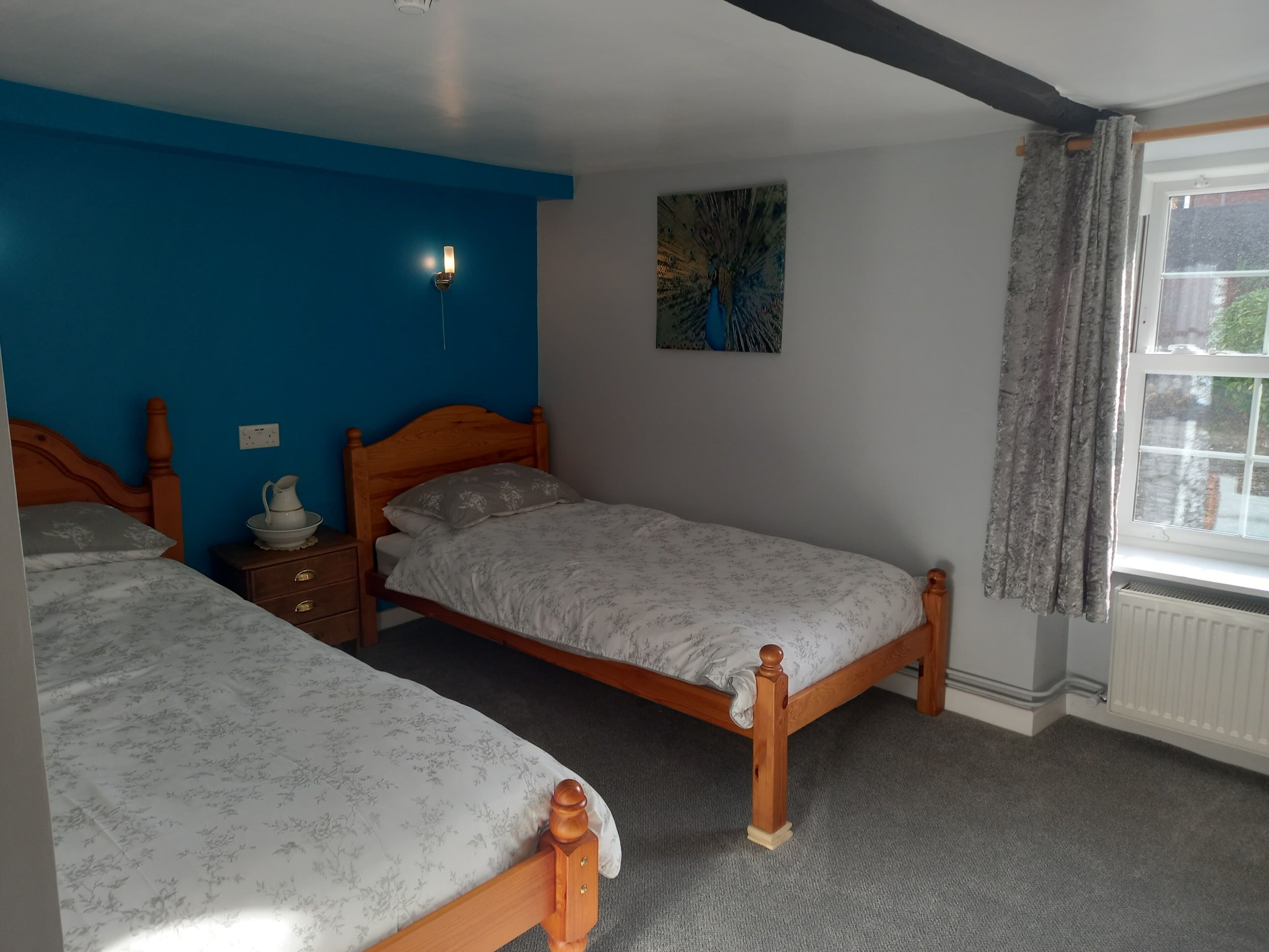 A bedroom with two wooden beds, a blue accent wall, a radiator, and a window with curtains.
