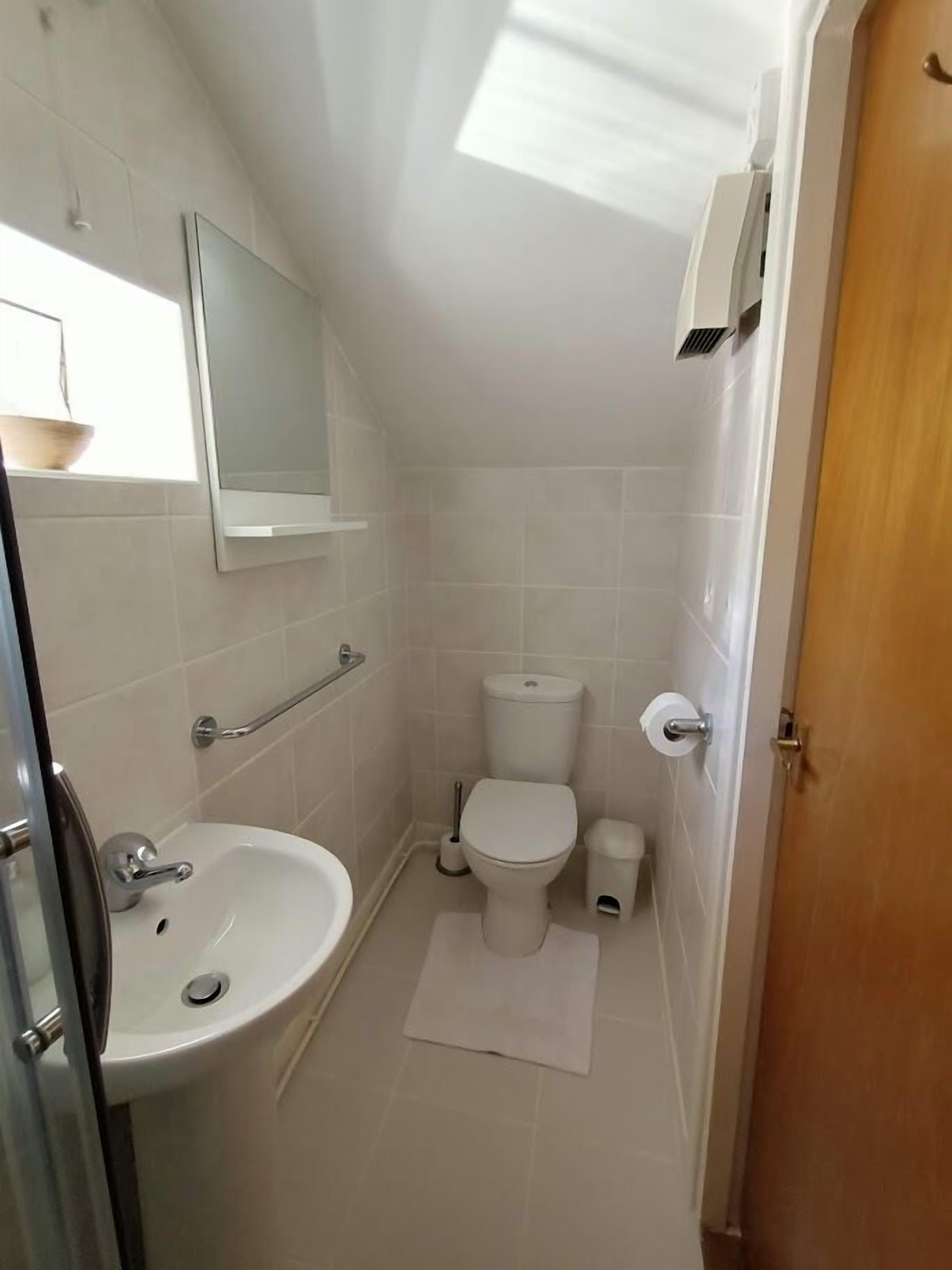 A small, white bathroom with a sink, toilet, and mirror.