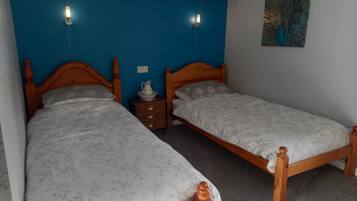 Una habitación con dos camas de madera, una mesita de noche y una lámpara fijada a la pared.