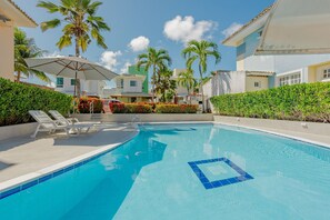 A swimming pool with lounge chairs, palm trees, and a clear blue sky.