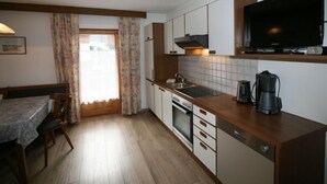 Una cocina compacta con horno integrado, cafetera y un televisor de pantalla plana sobre la encimera.
