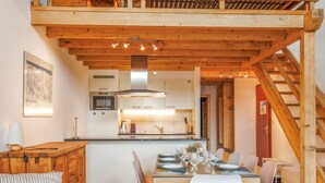 A modern kitchen with wooden beams, a dining area with white chairs, and a staircase. - Bietschorn 22 by Interhome (Nendaz)