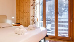 A bedroom with a bed, a nightstand, a lamp, and a view of a snowy outdoor area through a sliding glass door. - Bietschorn 22 by Interhome (Nendaz)