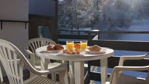 A breakfast table with croissants, muffins, and orange juice on a balcony with a snowy forest view. - Bietschorn 22 by Interhome (Nendaz)