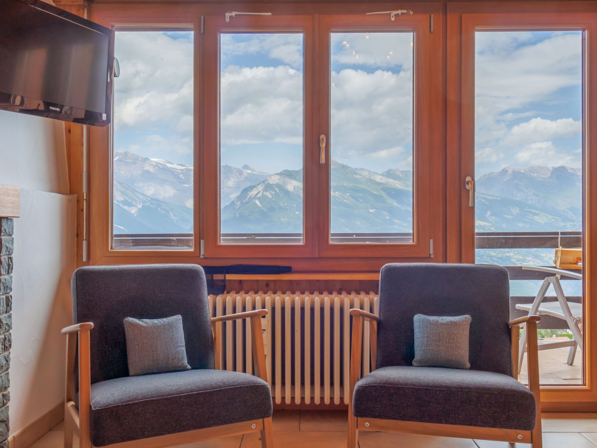 A room with two armchairs, a wooden radiator, and a TV mounted on the wall.
