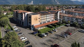 A multi-story building with a central courtyard, surrounded by a parking lot and residential buildings. - Cook P5/3 by Interhome (Le Bouveret)