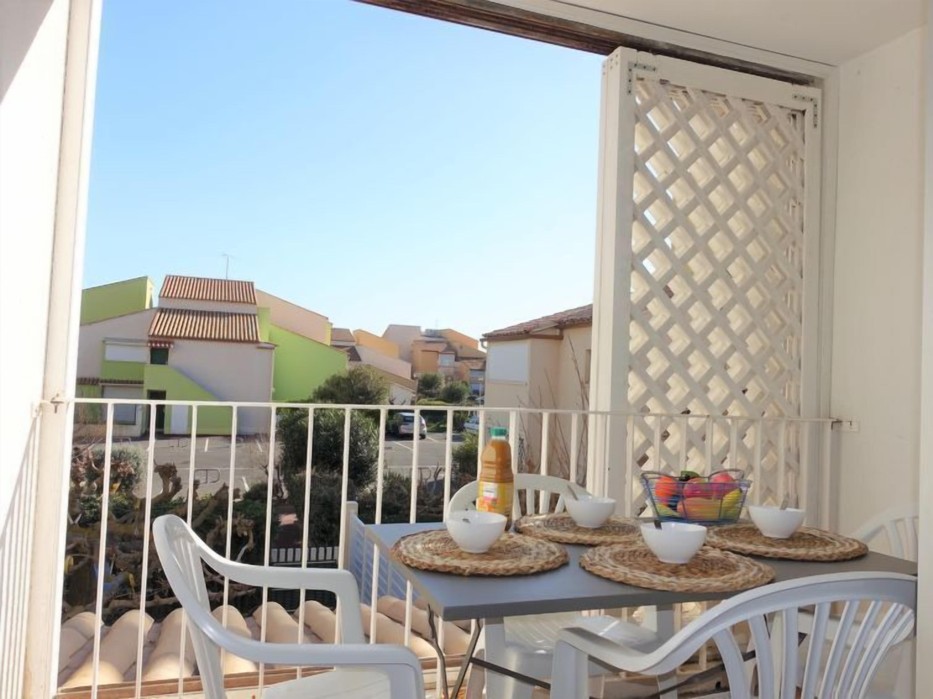 Un balcon avec une table dressée pour deux personnes, des chaises blanches et un paravent ajouré.