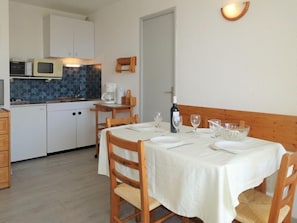 A compact kitchen with white cabinets, a microwave, and a coffee maker. A dining table with chairs is set for two, with wine glasses and a bottle on the table.