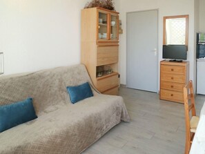A living room with a sofa, a wooden cabinet, a television, and a dining area.