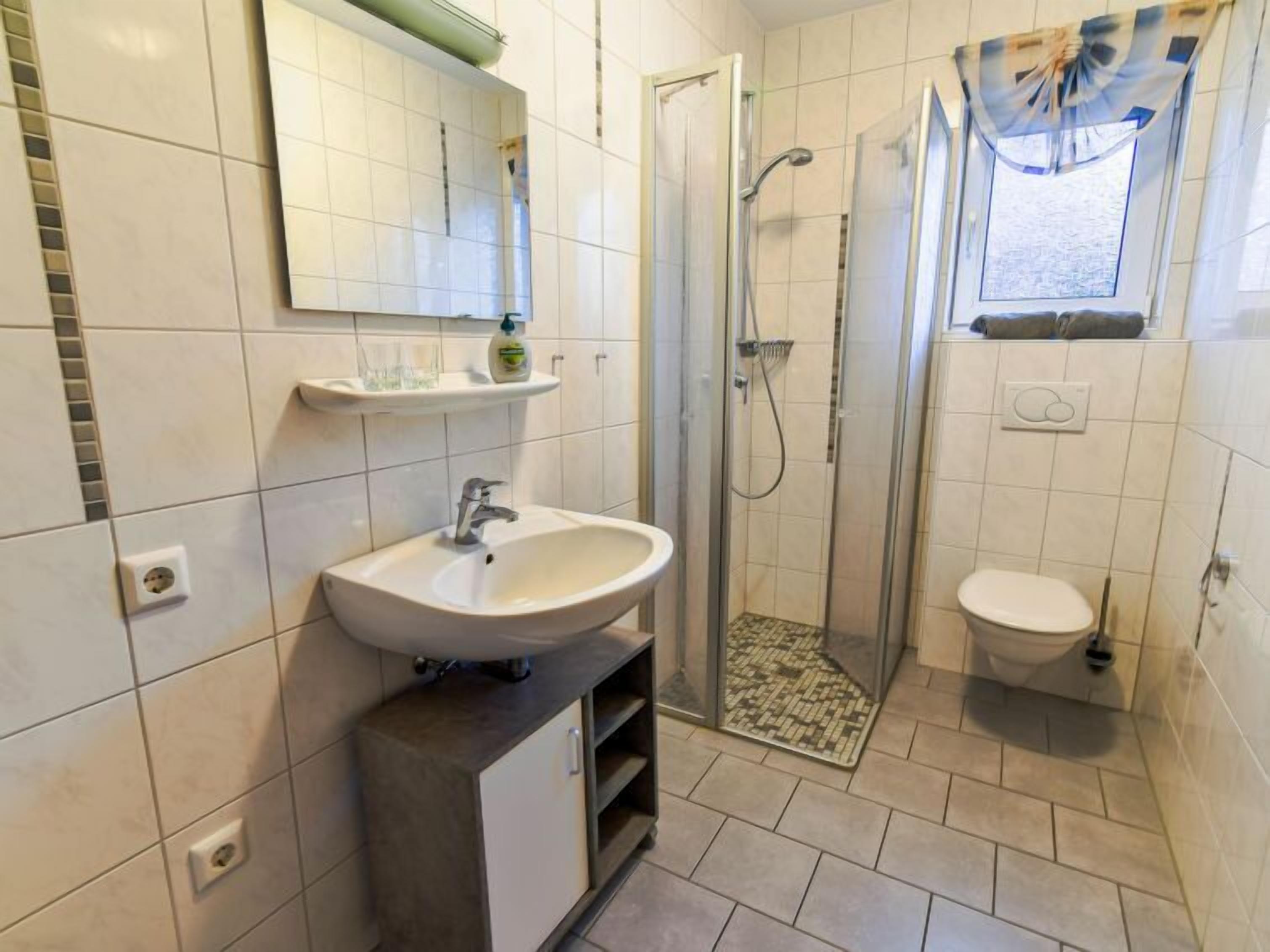 Une salle de bain équipée d’un lavabo, d’un miroir, d’une douche et de toilettes.