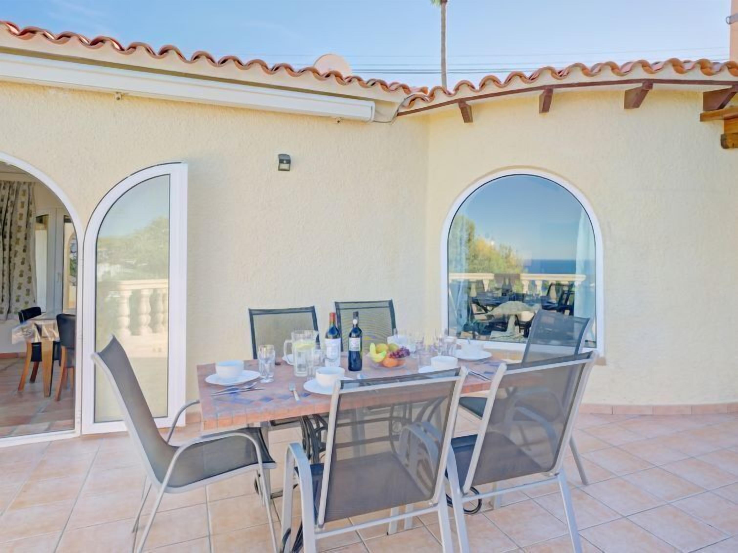 Una terrazza esterna con tavolo apparecchiato per mangiare, due ampie finestre ad arco e vista sul mare.