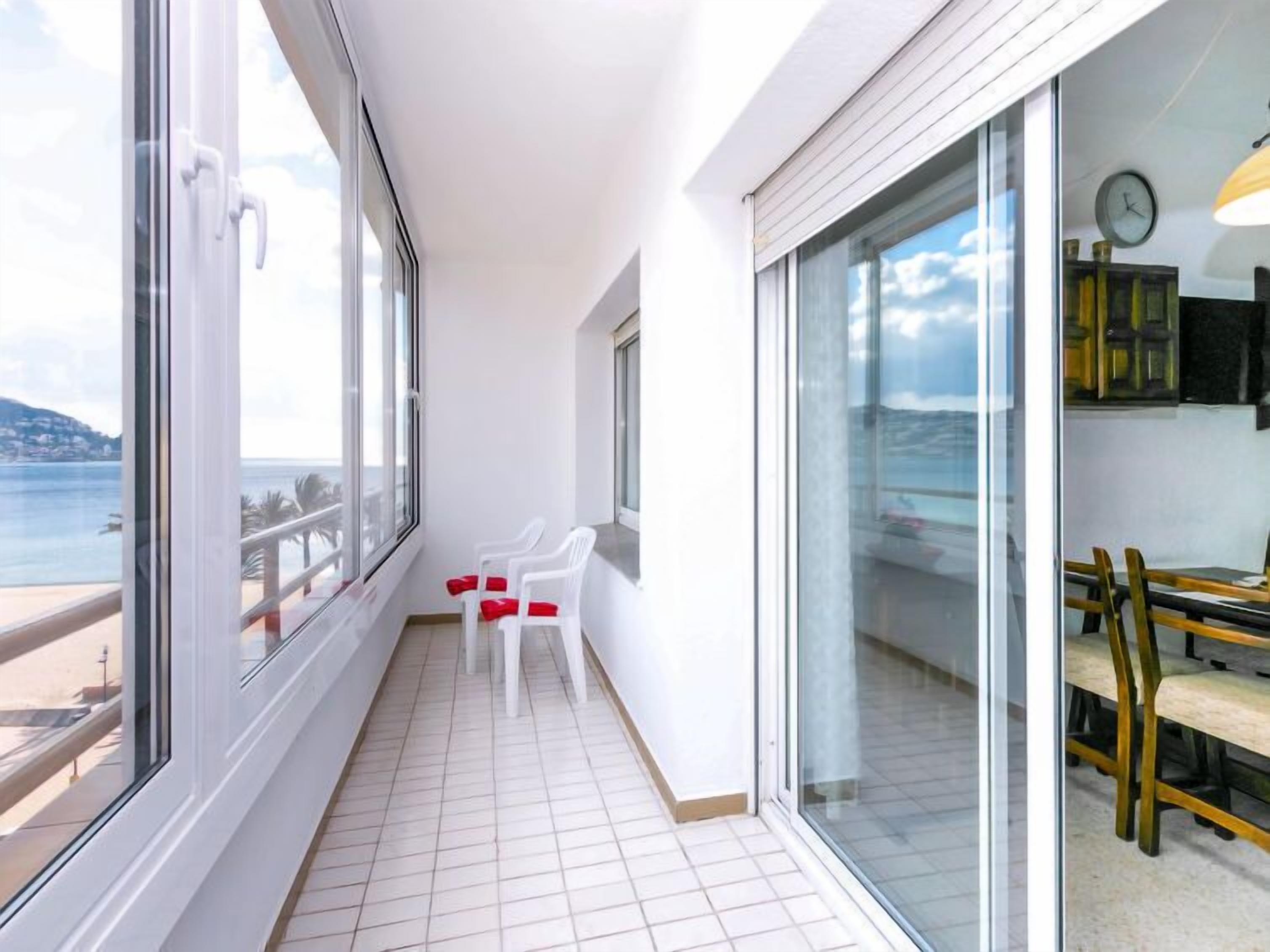 Een balkon met uitzicht op zee, vloer van witte tegels en een eethoek met stoelen en een tafel.
